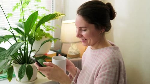 Woman Using Phone, Holding Coffee near Plants