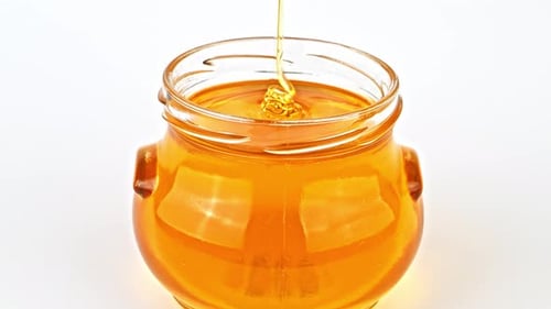 Golden Honey Dripping into Clear Glass Jar