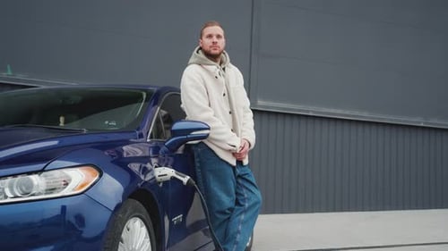 Man Leans on Electric Car While it Charges