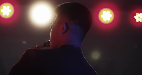 A young jazz musician wearing the black glasses , play saxophones on a stage in the club at night