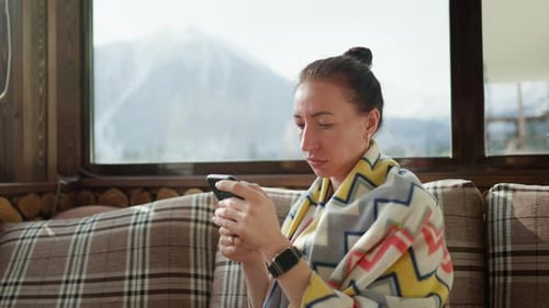 Pretty Woman Sitting on the Cafe Terrace on the Background of Winter Mountain Landscape Using a