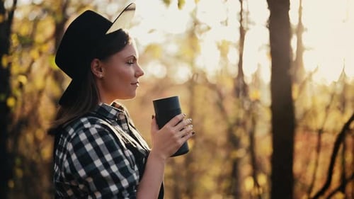 Hipster Woman Enjoys Aroma and Taste of Fresh Coffee Drinking From Thermos in Autumn Forest