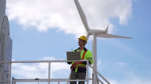 young male engineer working with laptop computer against wind turbine farm