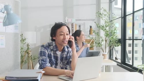 Two young Asian startup partners are working in a casual small business office.