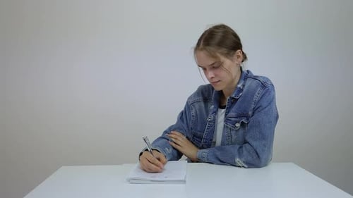 Pensive Young Adult Writing in Notebook at Desk