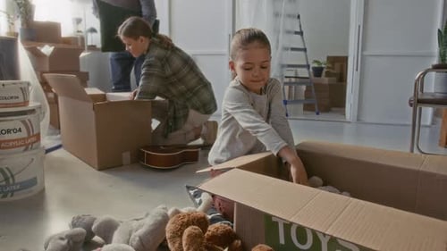 Menina colocando brinquedos macios em caixa de papelão durante a realocação