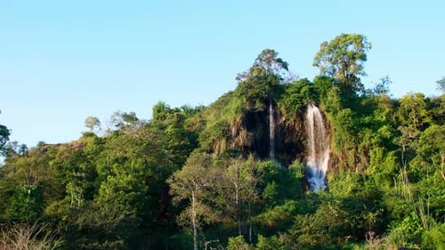A wide view of the natural waterfall that flows down the mountain is lit by the evening sun. Slow mo
