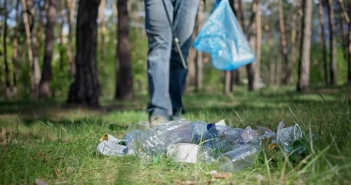Un hombre con una bolsa de plástico recoge basura en el bosque empalándola en un palo