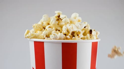 Popcornkörner, die einzeln auf weißem Hintergrund in einen rot-weiß gestreiften Eimer fallen
