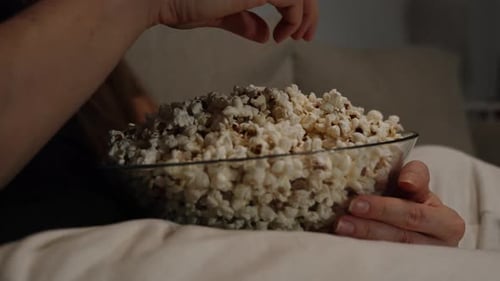 Close-Up of the Bowl of Popcorn Woman Holds and Eats Sitting on the Sofa in Front of the TV in the D