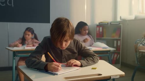 Konzentriertes Schreiben eines Schülers in ein Notizbuch im Schulunterricht. Nachdenklicher Junge mit Stift
