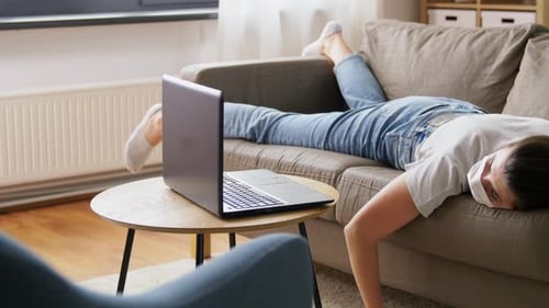 Tired person lying on couch using laptop