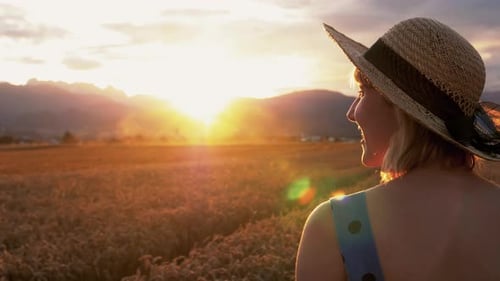A following shot of a young female gently touching the grains of wheat and smiling while walking.