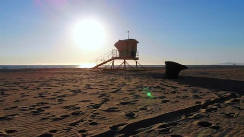 Low, fast fly around lifeguard tower and trash can to beautiful ocean waves and sunset in Huntington