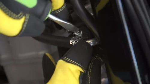 Gloved hands seen tightening a fuel line clamp on a motorcycle with a screw driver - close up