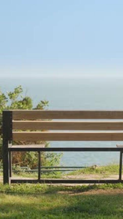 Eine leere Holzbank an der Küste. Blick aufs Meer. Sommer, sonniger Tag, Urlaub. Vertikal. Soziale Medien