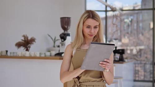 Female Blonde Salesperson Holding a Tablet Takes Orders for Her Coffee Shop