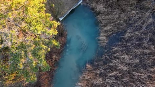 Aerial drone view of a narrow Michigan stream flowing between forested banks, ideal salmon spawning