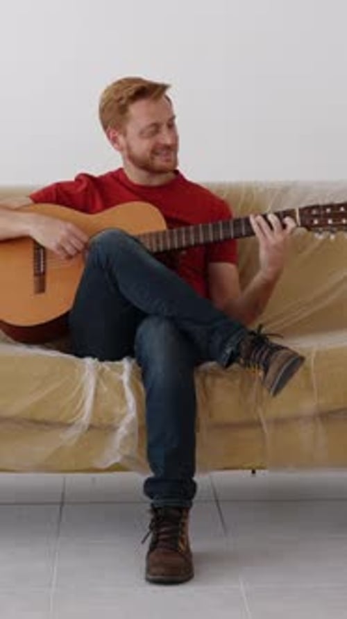 Cheerful Young Man Playing the Guitar at New Home