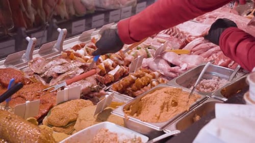 A gloved deli worker selects a portion of fresh cut meat from a specialty counter