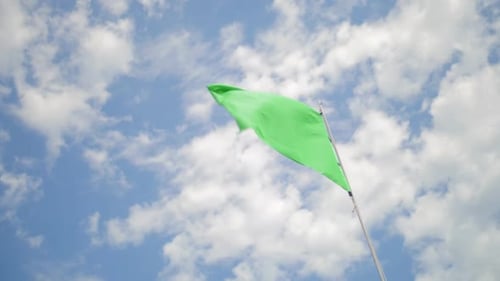 Green Flag Waving against Blue Sky and Clouds