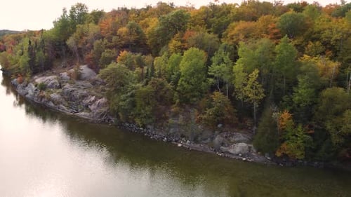 Aerial landscape view over a river flowing by colorful autumnal trees, with yellow red and orange fo