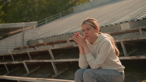Woman Sits Thoughtfully on Bleachers Outdoors