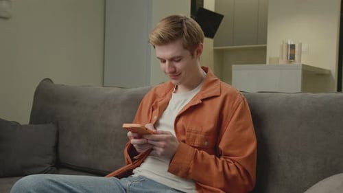 Smiling Young Adult Using Phone on Couch