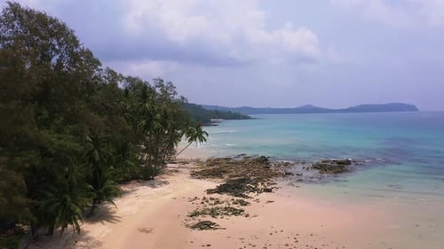 Tropical Koh Kood sand beach with palm trees and turquoise ocean waves.