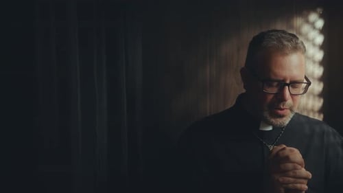 Clergyman Praying in Dimly Lit Confessional Booth