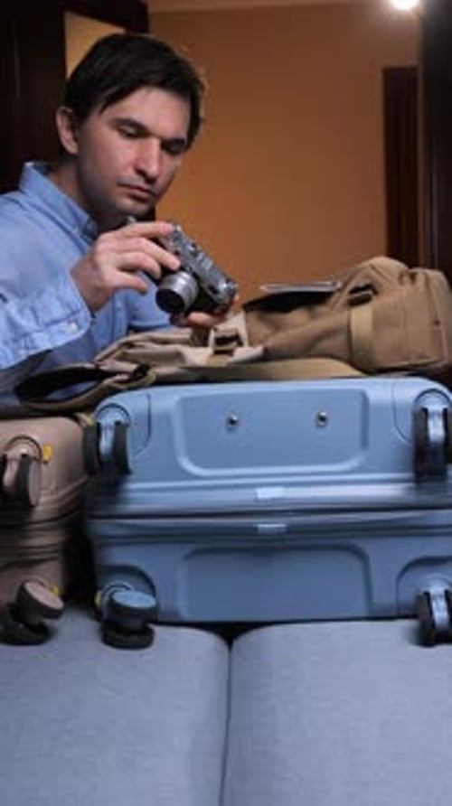 Man Inspecting Camera with Luggage in Room