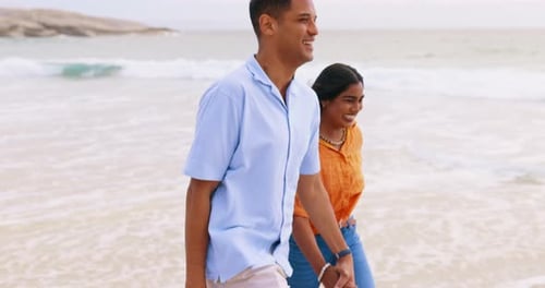 Happy couple, walking and holding hands while laughing on the beach for vacation