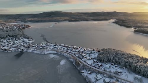 Aerial sunset over a snowy village and frozen lake