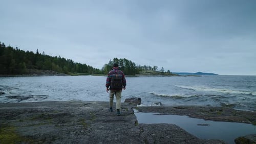 Genießen Sie die Schönheit der Natur beim Wandern: Lonely Man Tourist mit Rucksack, der alleine an der Seeküste spazieren geht