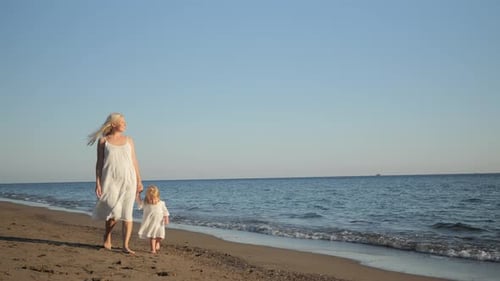 Mom and Daughter Walk Hand in Hand Along the Sea Beach Along the Sea