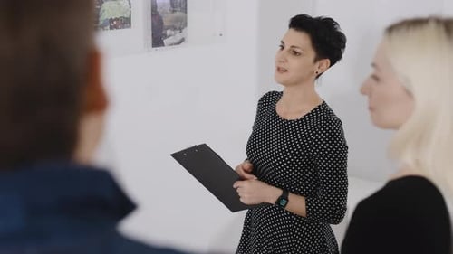A Woman Gallery Owner Tells Visitors About the Paintings Presented at the Exhibition