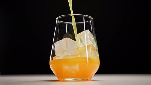 Orange Juice Being Poured Over Ice in Glass