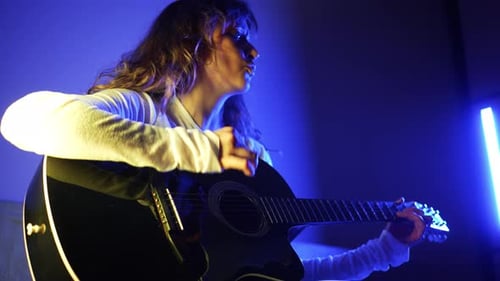 Female Musician Performing Acoustic Guitar Illuminated By Blue Neon Light Creating Moody Artistic