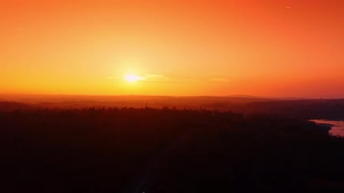 Amazing burning sunset in the countryside. Cars ride by the road in the forest.