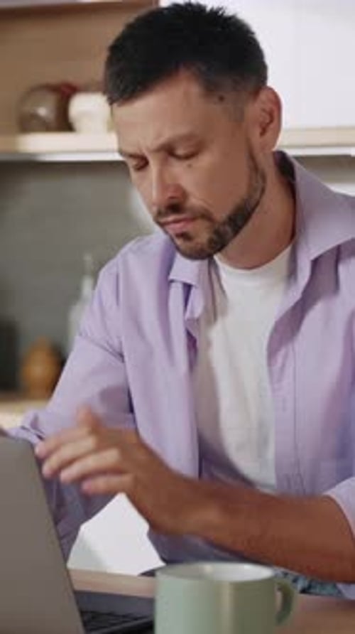Man Rubs Temples While Working on Laptop