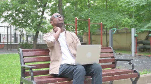 Man Uses Laptop in Park and Massages Neck