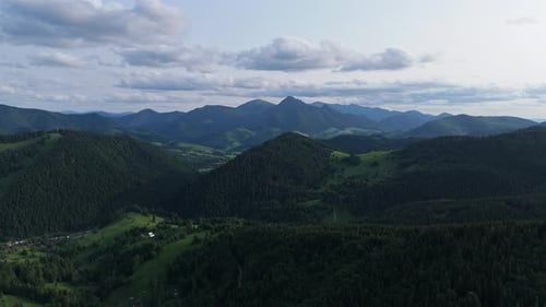 Aerial View of Green Mountain Valley with Forest Hills and Distant Peaks Under Clouds