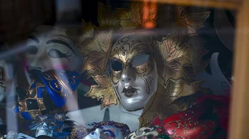 Beautiful Venetian Carnival Masks displayed in a shop in Venice with reflection of people passing by
