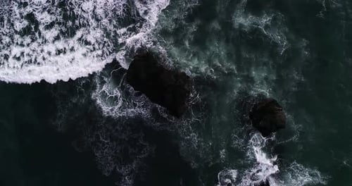 Aerial of the ocean waves washing up on a black basalt rock in Bali move left