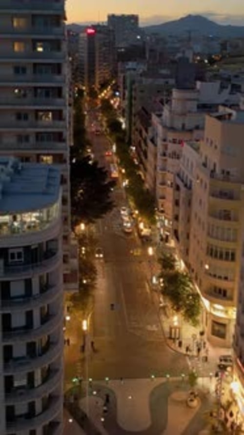 Aerial drone view of cars moving between the buildings in Alicante, Spain at sunset. Vertical