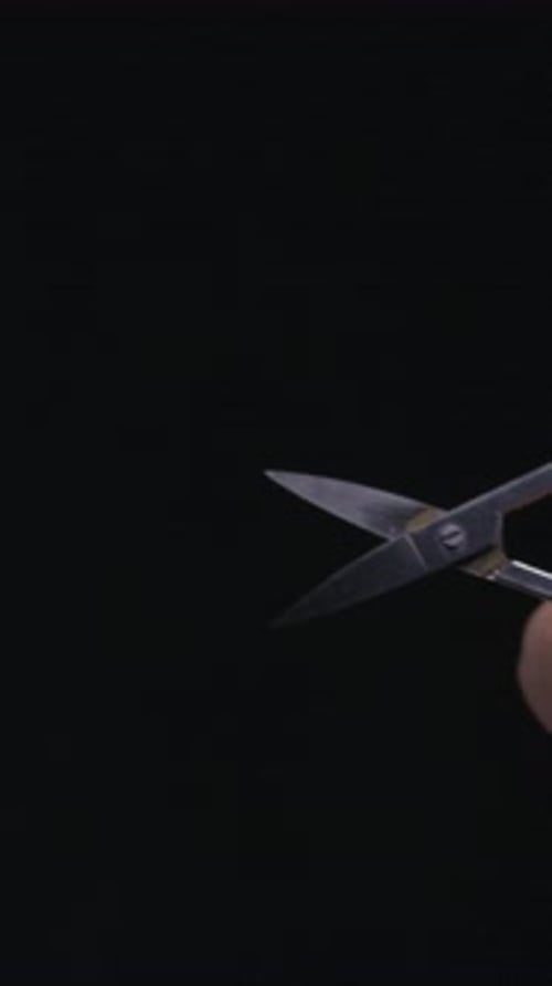 Close Up Hand Holding Small Scissors Against Black Background