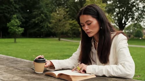 Vista lateral de la mujer leyendo un libro y tomando café afuera.