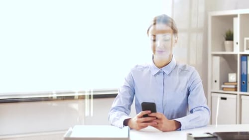 Businesswoman at office types on smartphone through glass wall technology