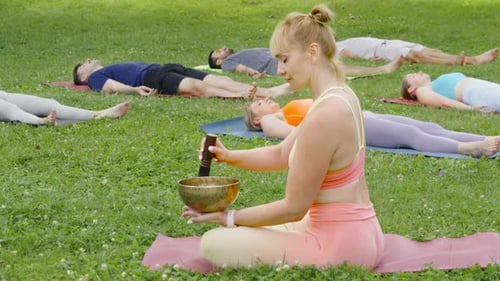 Young Woman Playing Singing Bowls During Yoga Meditation in Sunny Summer Park