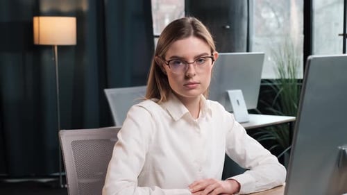 Businesswoman Sits at Desk and Stares into Camera